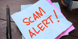 desktop with a pen and sticky note that says Scam Alert