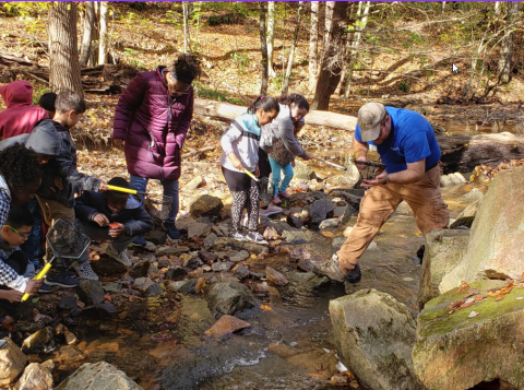 Photo of students and teacher at a stream checking the quality of the water.
