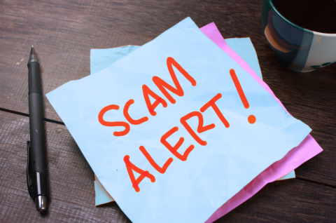 desktop with a pen and sticky note that says Scam Alert